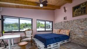 A bedroom with a stone wall, a bed with blue bedding, a wooden ceiling fan, and a table with a chair. - Istrian Tavern with Shared Pool (Banjole)