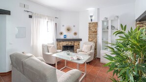 Een woonkamer met een open haard, een glazen salontafel en een witte fauteuil.