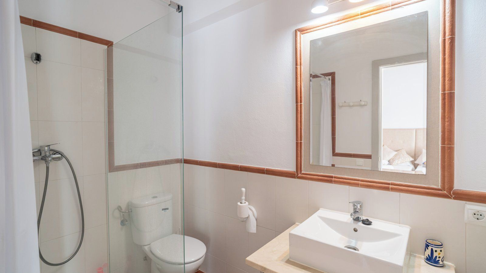Een badkamer met een douchecabine van glas, een toilet en een wastafel met een spiegel erboven.