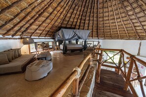 A thatched-roof room with a bed, a sofa, and a wooden railing.
