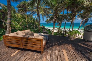 A wooden deck with a bed, surrounded by palm trees and a view of the ocean.