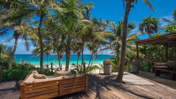 A wooden deck with a bench, palm trees, and a view of the ocean. - CASA ZABA (Tulum)