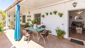 An outdoor patio with a glass table and chairs, surrounded by potted plants and a blue curtain.