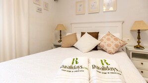 A neatly made bed with white linens and two towels with the logo "Ruralidays.com" and text "Your home in Andalusia".