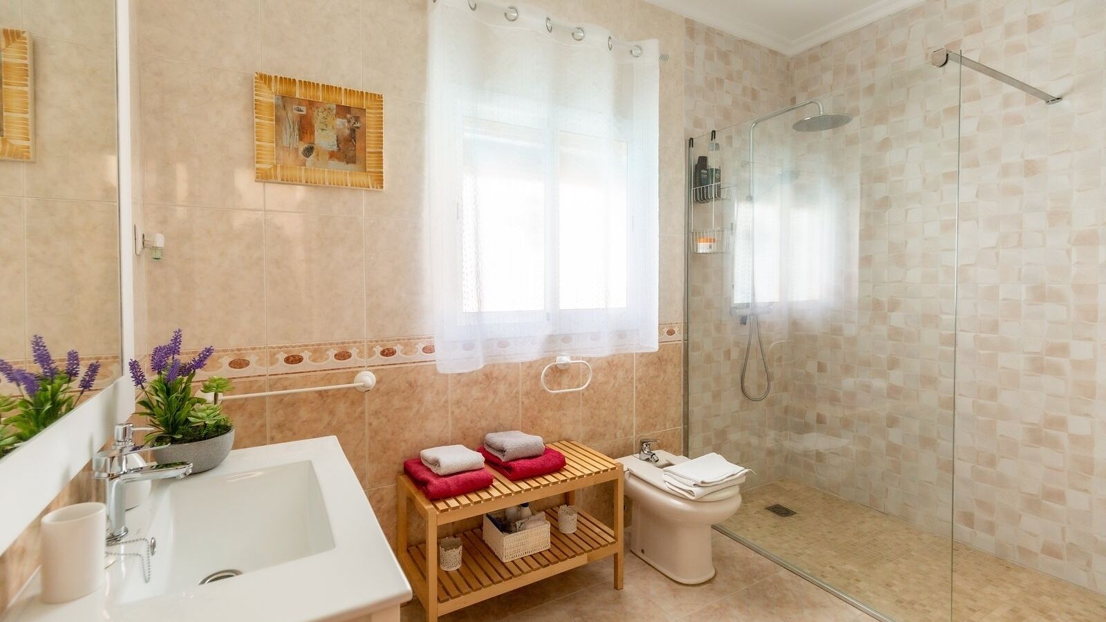 A modern bathroom with a bathtub, shower, and toilet. There are towels and a small shelf with toiletries.