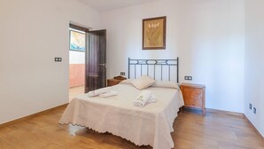 A bedroom with a bed, a wooden nightstand, a framed picture on the wall, and a door leading to another room. - Villa Ortega Alba Alcalá La Real by Ruralidays (Jaén)