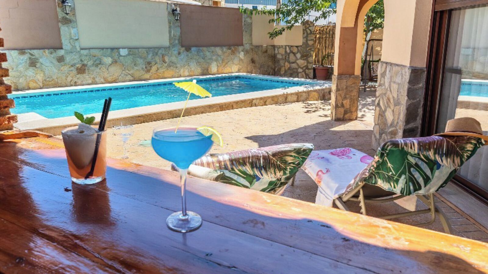 Eine Poolbar mit einem Getränk und zwei Liegestühlen.