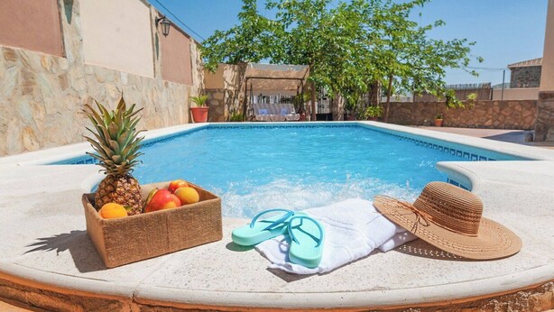 A swimming pool with a fruit basket, flip-flops, and a straw hat on the edge. - Villa Ortega Alba Alcalá La Real by Ruralidays (Jaén)