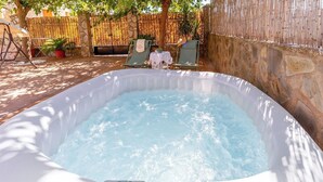 A hot tub in a stone-walled outdoor area with a bamboo fence, two lounge chairs, and a small table with a white tablecloth. - Villa Ortega Alba Alcalá La Real by Ruralidays (Jaén)