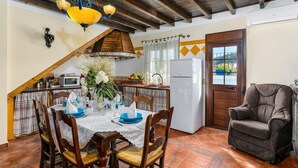 A dining area with a table set for four, a kitchen with a refrigerator, and a wooden ceiling. - Casa de Teones con piscina privada Montecorto by Ruralidays (Málaga)