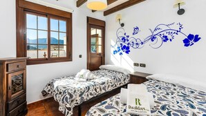 A bedroom with two beds, wooden furniture, a decorative wall, and a view through a window. - Casa de Teones con piscina privada Montecorto by Ruralidays (Málaga)