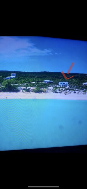 Vista de la playa con varios edificios, incluyendo una casa moderna y una estructura más grande con techo inclinado.