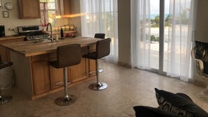 A modern kitchen with a central island, bar stools, and a view of the beach through large windows. - Ocean Front facing the Tropic of Cancer Beach !! (Little Exuma)