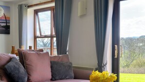 A living room with a sofa, a vase of flowers, and a view of a green landscape through a window. - Cosy cottage with designated parking. (Whitby)
