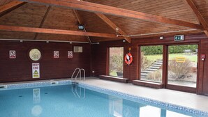 An indoor swimming pool with wooden beams, safety signs, and a lifebuoy. - Cosy cottage with designated parking. (Whitby)