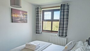 A bedroom with a bed, a radiator, a window with curtains, and a painting on the wall. - Cosy cottage with designated parking. (Whitby)
