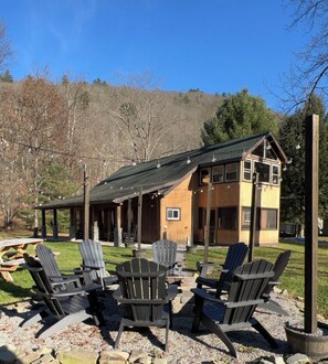 A lodge with a covered patio area, outdoor seating, and a view of a forested hill. - Elk/trout/hunting/star gazing 4 bdrm, 2 bath cabin (Austin)