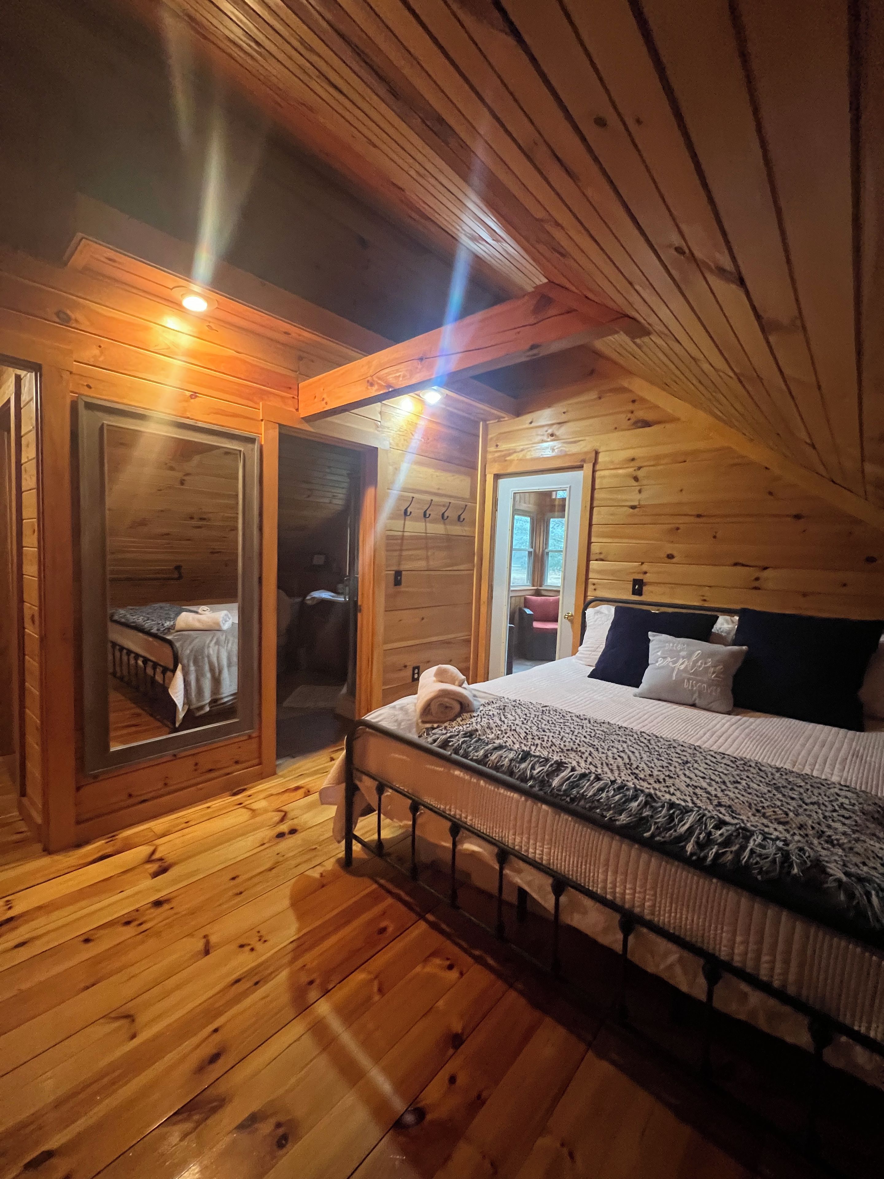 Un dormitorio de cabaña de madera con una cama, un espejo y una puerta que da a otra habitación.