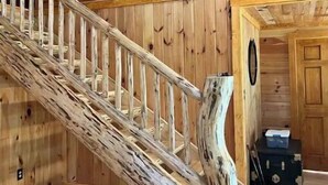 A wooden staircase with a compass design on the wall, a rustic wooden handrail, and a small chest of drawers in the corner.