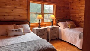 A cabin room with two beds, wooden walls, a window, and a mounted deer head.