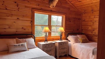 Cozy cabin-style room with two single beds, a mounted deer head, and a large window offering a view of the outdoors.