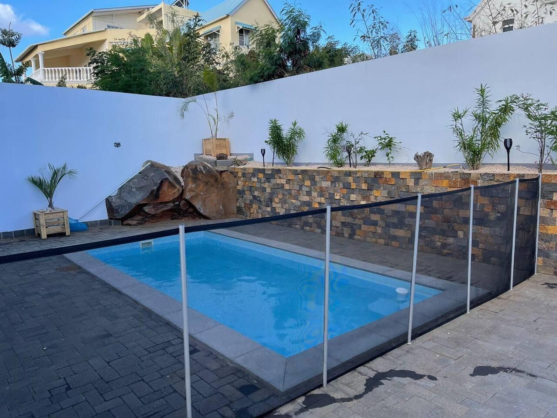 A swimming pool with a stone wall and a white fence.