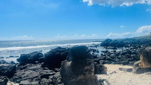 Costa rochosa com ondas quebrando na praia sob um céu claro.