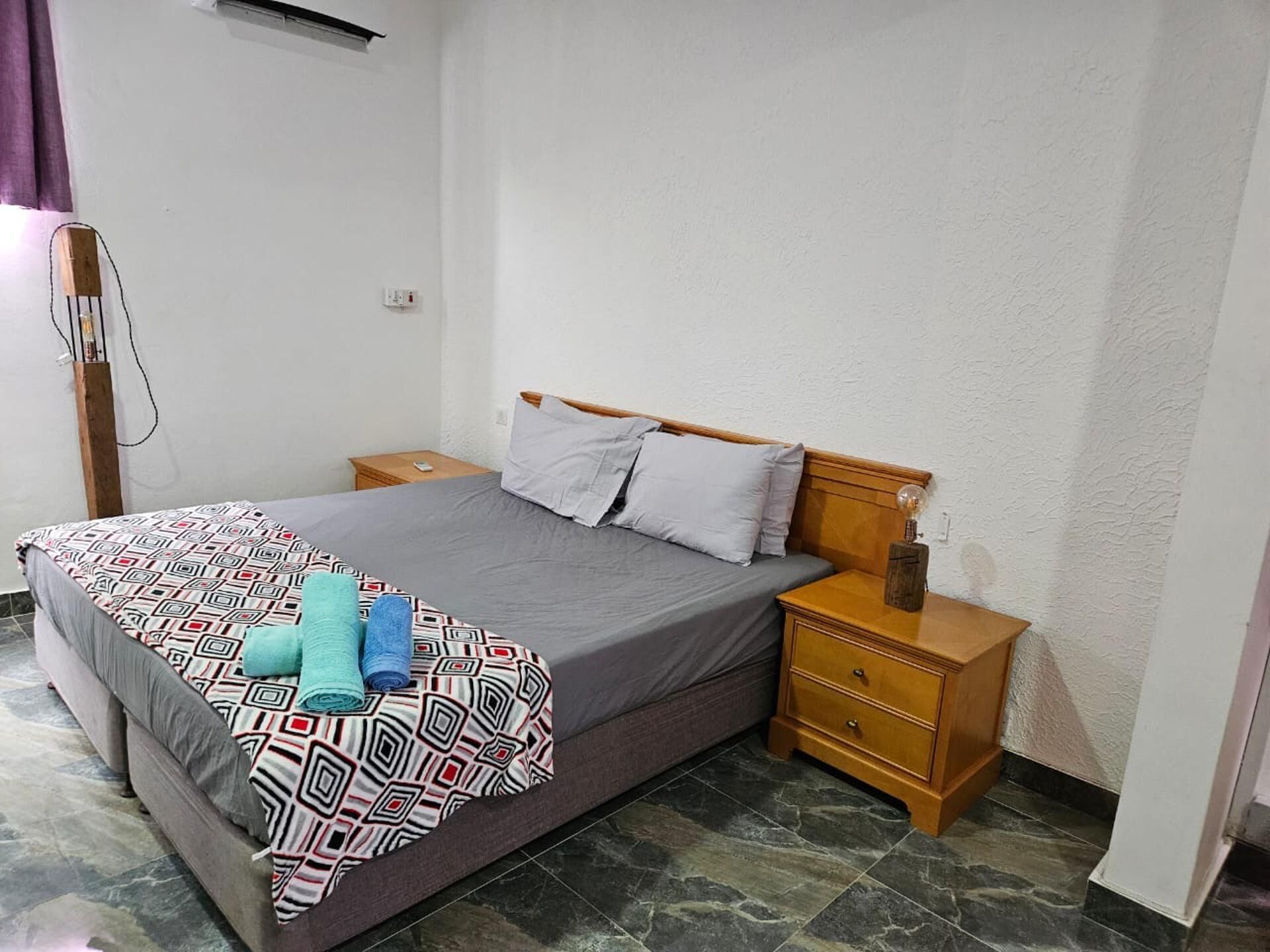 Een keurig opgemaakte slaapkamer met een bed, twee nachtkastjes en een bijzetmeubel.