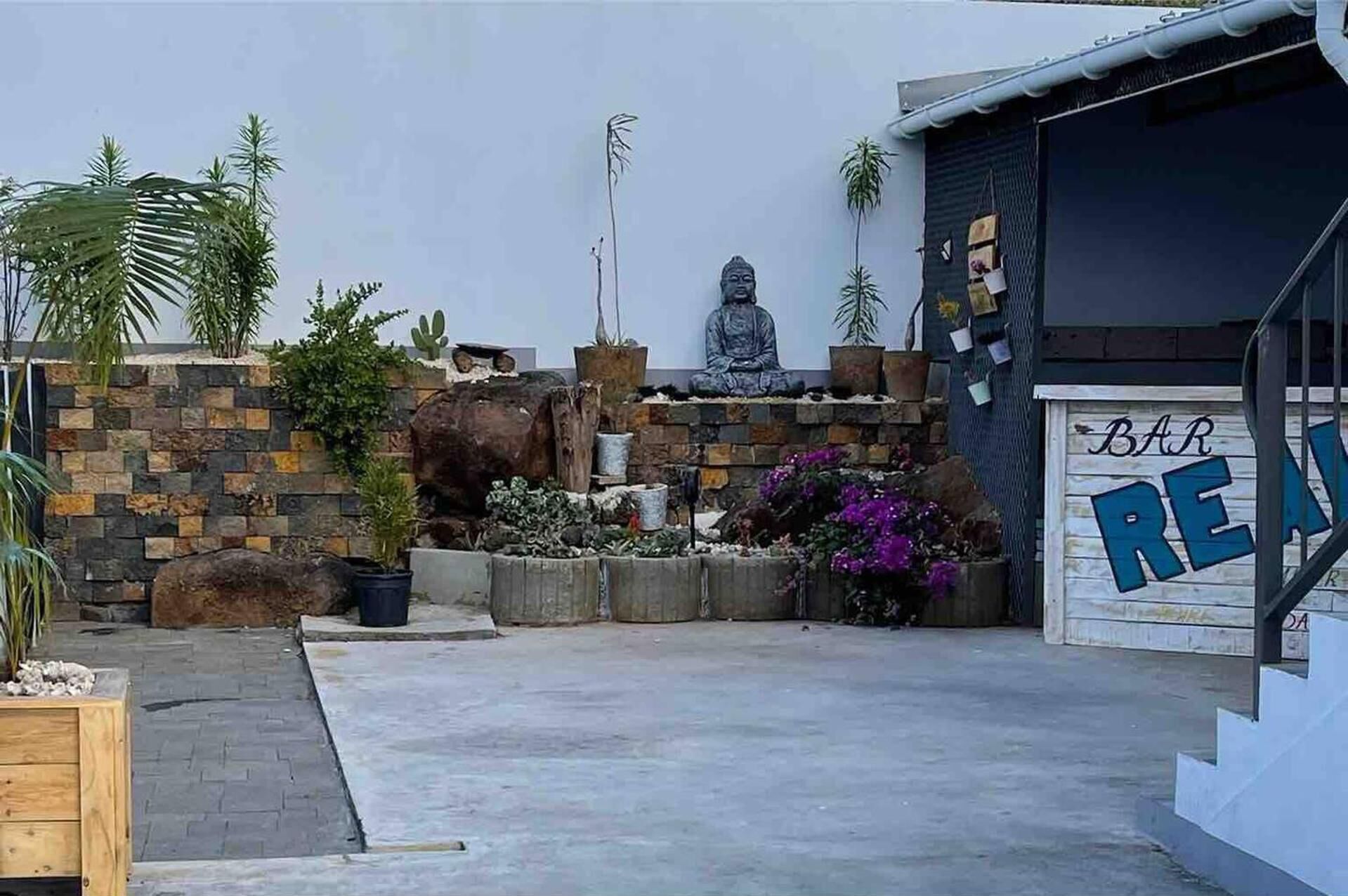 En moderne bygning med en meditationsstatue, en stenvæg og en garage med et skilt der siger 'BAR'.