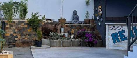 En moderne bygning med en meditationsstatue, en stenvæg og en garage med et skilt der siger 'BAR'.