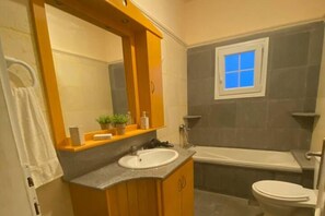 Ein Badezimmer mit Waschbecken, Spiegel und einem Fenster über der Badewanne.