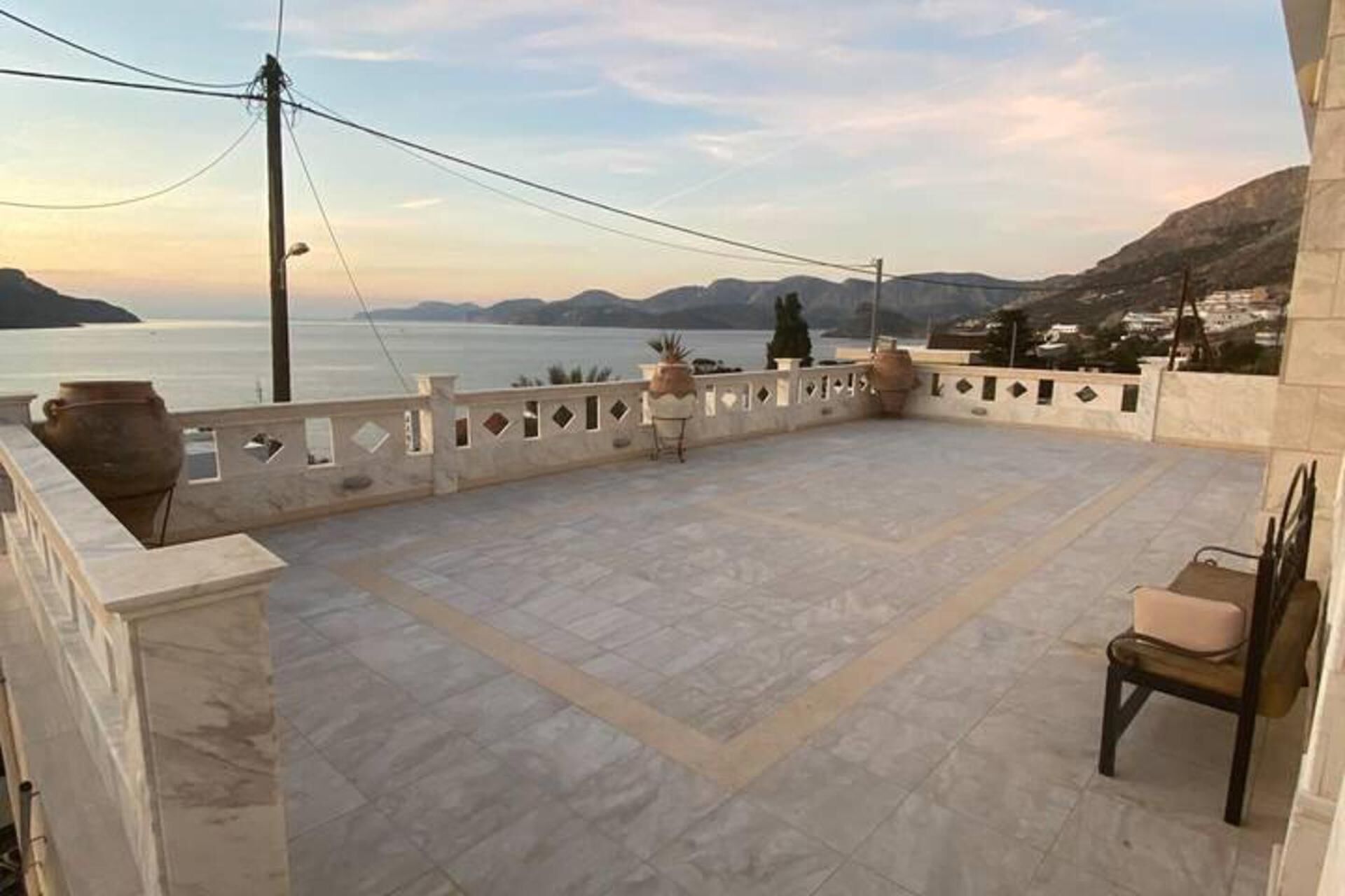 Une terrasse offrant une vue sur la mer et les montagnes, avec un sol carrelé et une chaise.