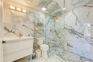 A bathroom with a marble wall, a glass shower enclosure, a white sink, and a toilet. - Anna Maria Beach Serenity (Anna Maria)