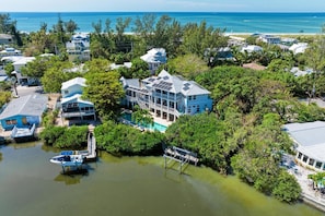 A large house with multiple levels and a pool, surrounded by dense greenery and a body of water. - Anna Maria Beach Serenity (Anna Maria)