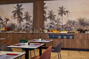 Restaurante con barra de buffet, paredes de madera y un mural tropical. Las mesas están preparadas con servilletas rojas y caminos de mesa blancos.