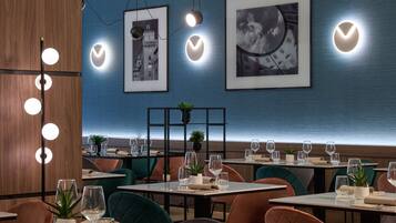 Ein modernes Restaurant-Interieur mit gedeckten Tischen, gerahmten Bildern an der Wand und Pendelleuchten.