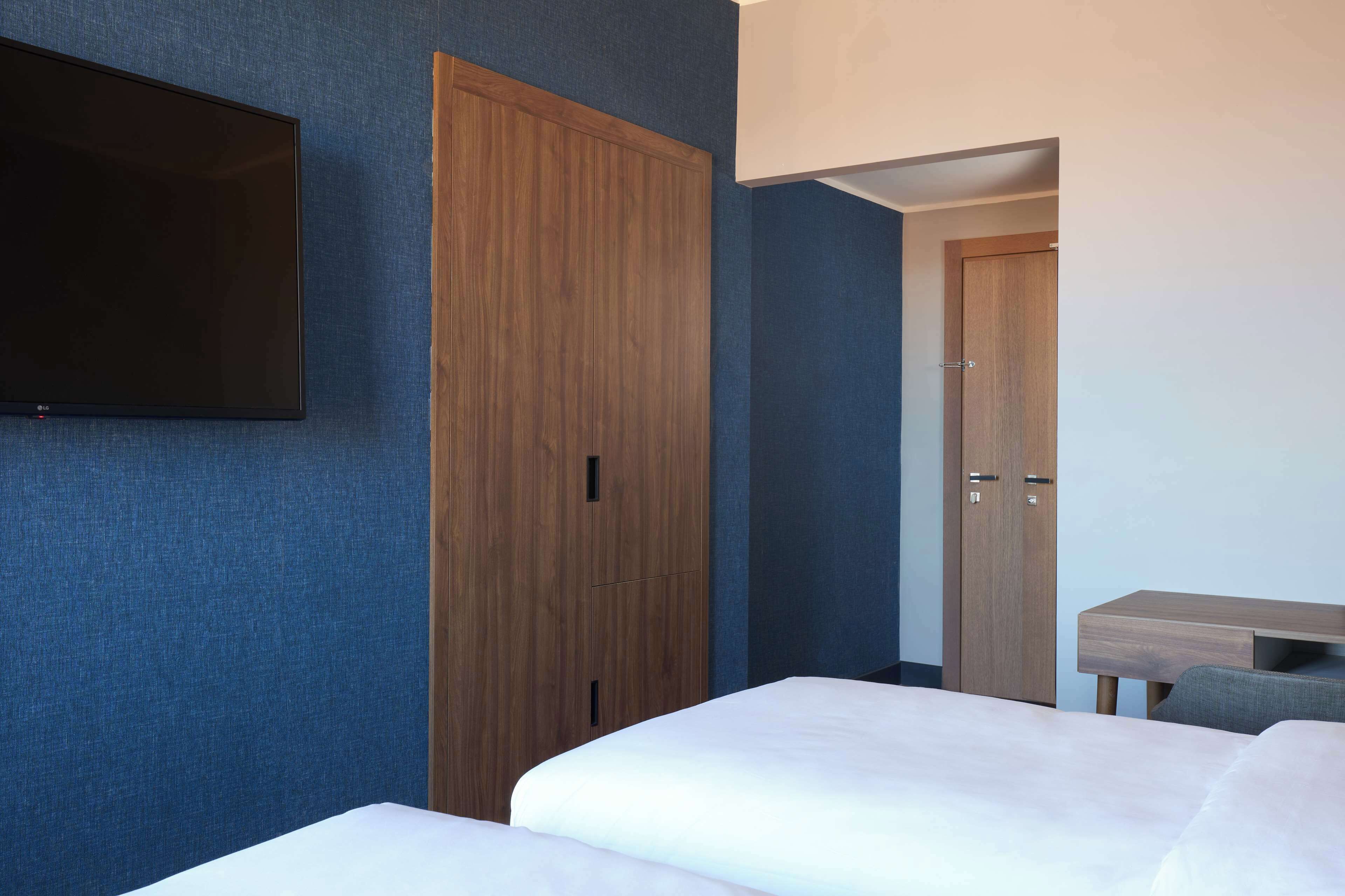 Habitación de hotel con un armario grande, un televisor de pantalla plana en la pared y un escritorio con una silla.