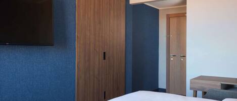 Habitación de hotel con un armario grande, un televisor de pantalla plana en la pared y un escritorio con una silla.