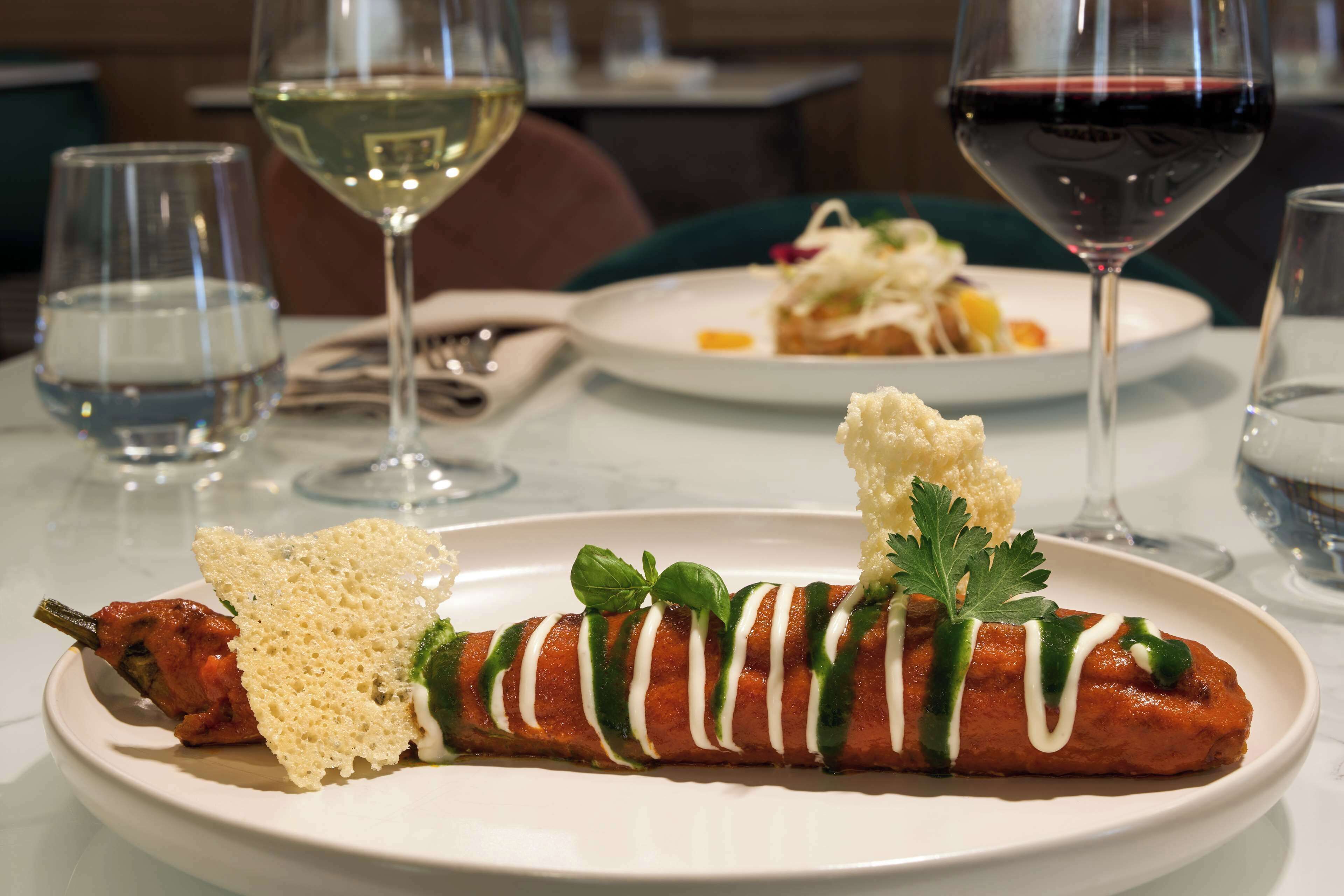 A plate with a rolled meat dish, garnished with herbs and sauce, accompanied by bread and a glass of white wine.