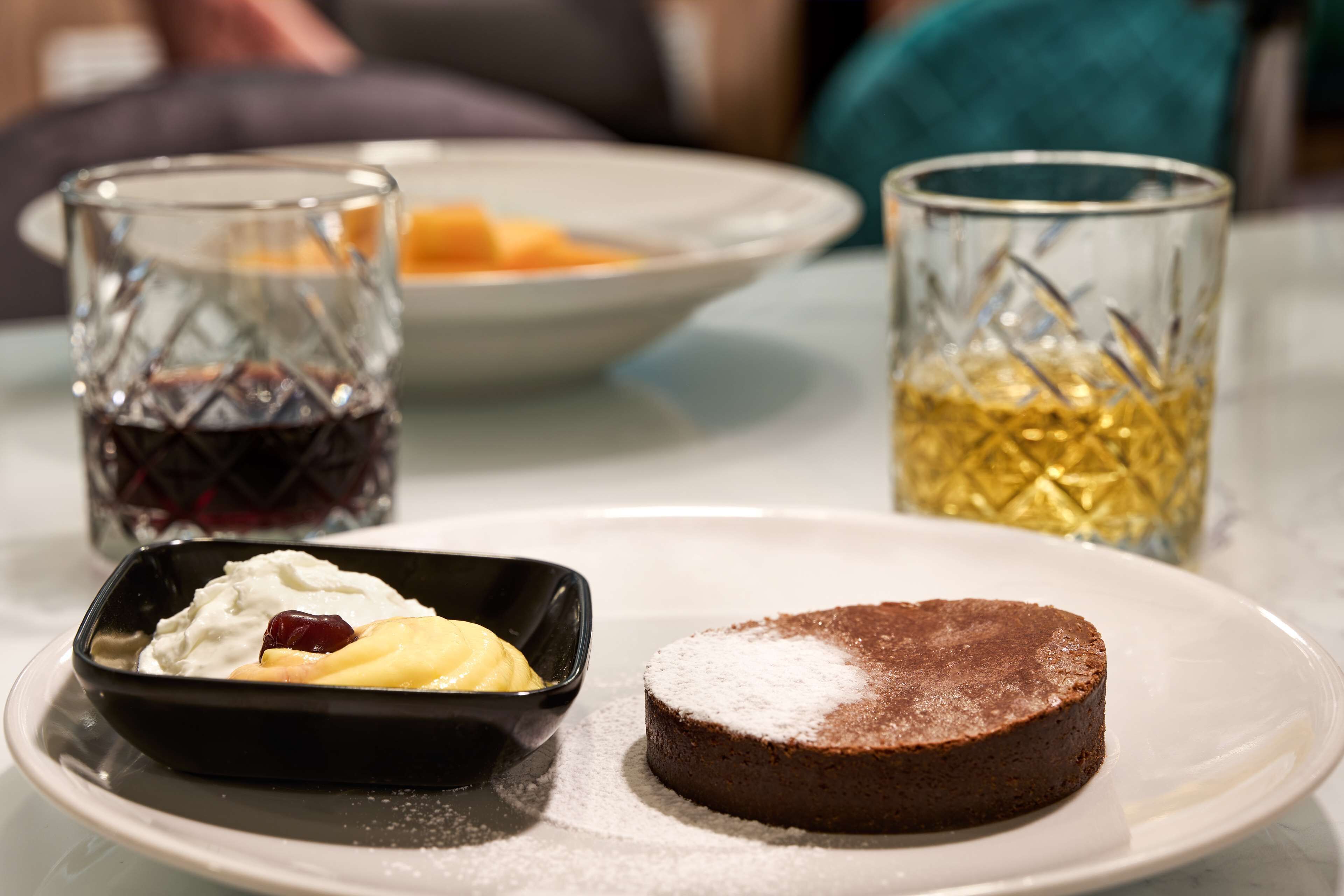 Un plat de postres amb una mica de pastís de xocolata i un bol petit de nata amb fruita.