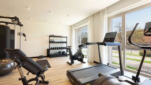 A gym with treadmills, a stationary bike, and a rowing machine. There are dumbbells and a weight rack in the background. - Radisson Hotel Ferrara (Ferrara)