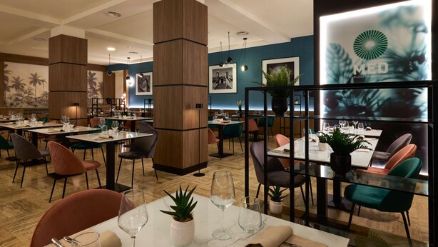 A modern restaurant interior with wooden pillars, tables with chairs, and framed pictures on the walls. - Radisson Hotel Ferrara (Ferrara)