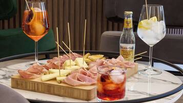 Een tafel met diverse soorten eten en drinken, waaronder een fles tonic, een glas rode drank en een glas met citroenpartjes en ijs.