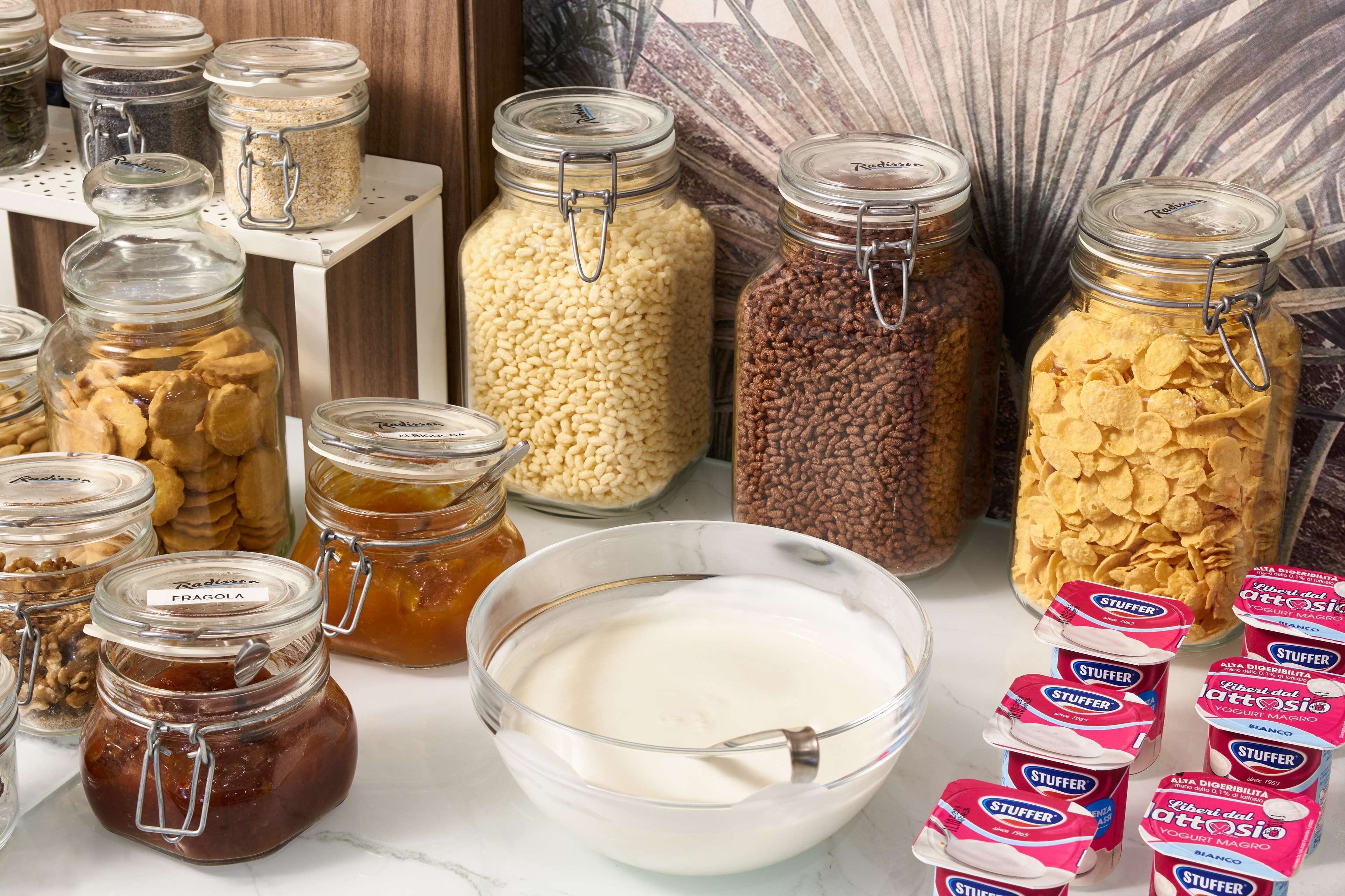 Various food items in jars and a bowl of yogurt on a table.