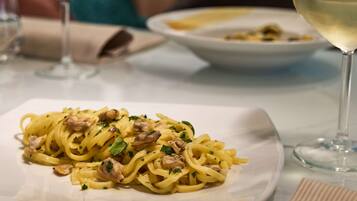 Un piatto di pasta con funghi e erbe aromatiche, un bicchiere di vino bianco e una tovaglietta su un tavolo.