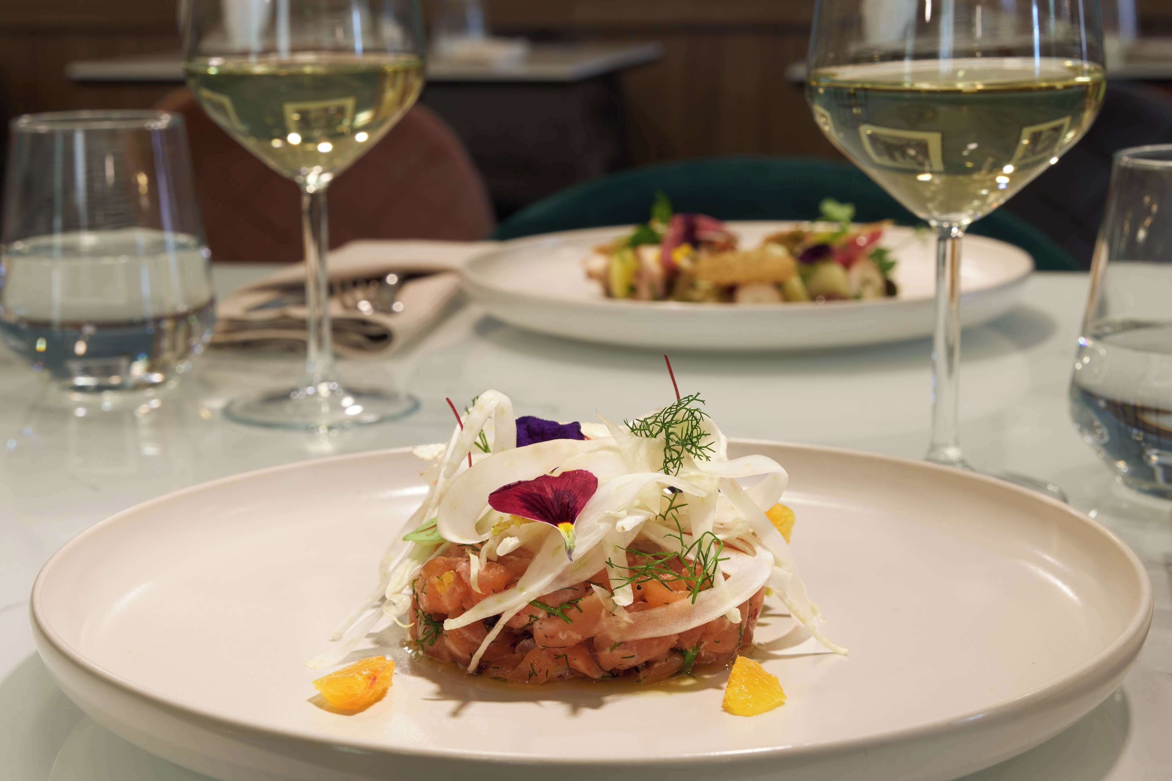 A dining table with a plate of food and two glasses of white wine.