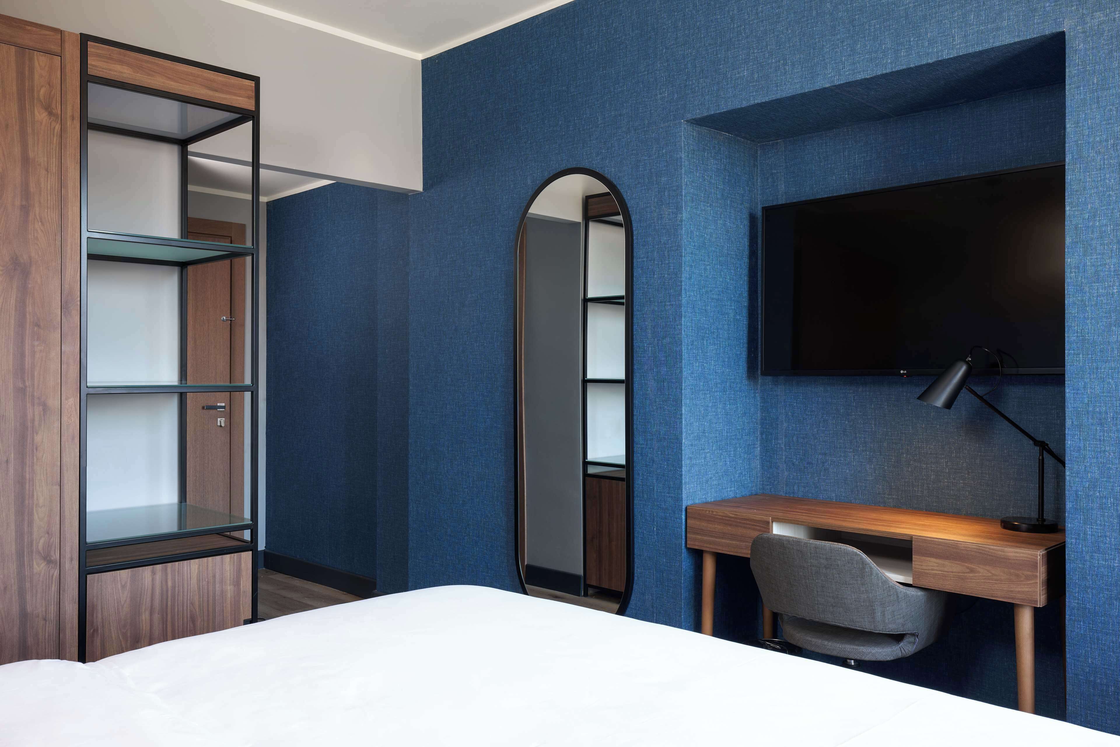 Une chambre d’hôtel comprenant un lit, un bureau avec une chaise, une télévision et une armoire avec des étagères.