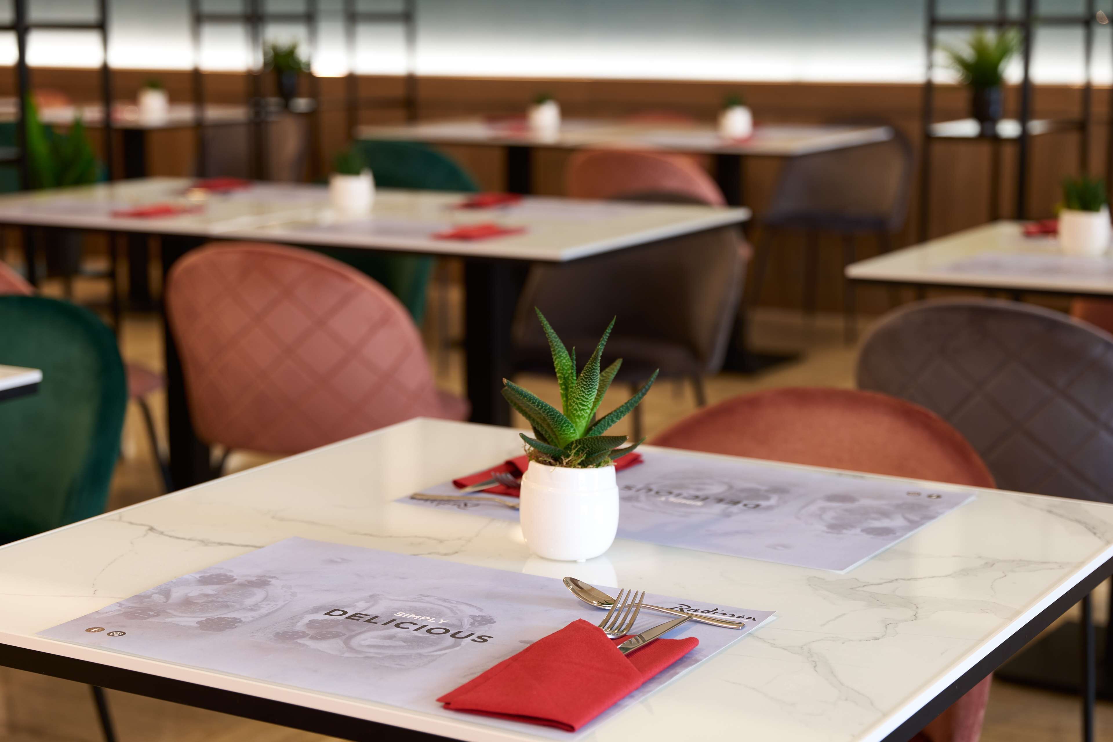 A restaurant interior with tables set for dining, featuring a potted plant and a menu.