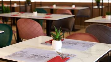 Interior de un restaurante con mesas dispuestas para comer, destacando una planta en maceta y un menú.