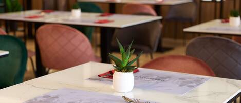 A restaurant interior with tables set for dining, featuring a potted plant and a menu.
